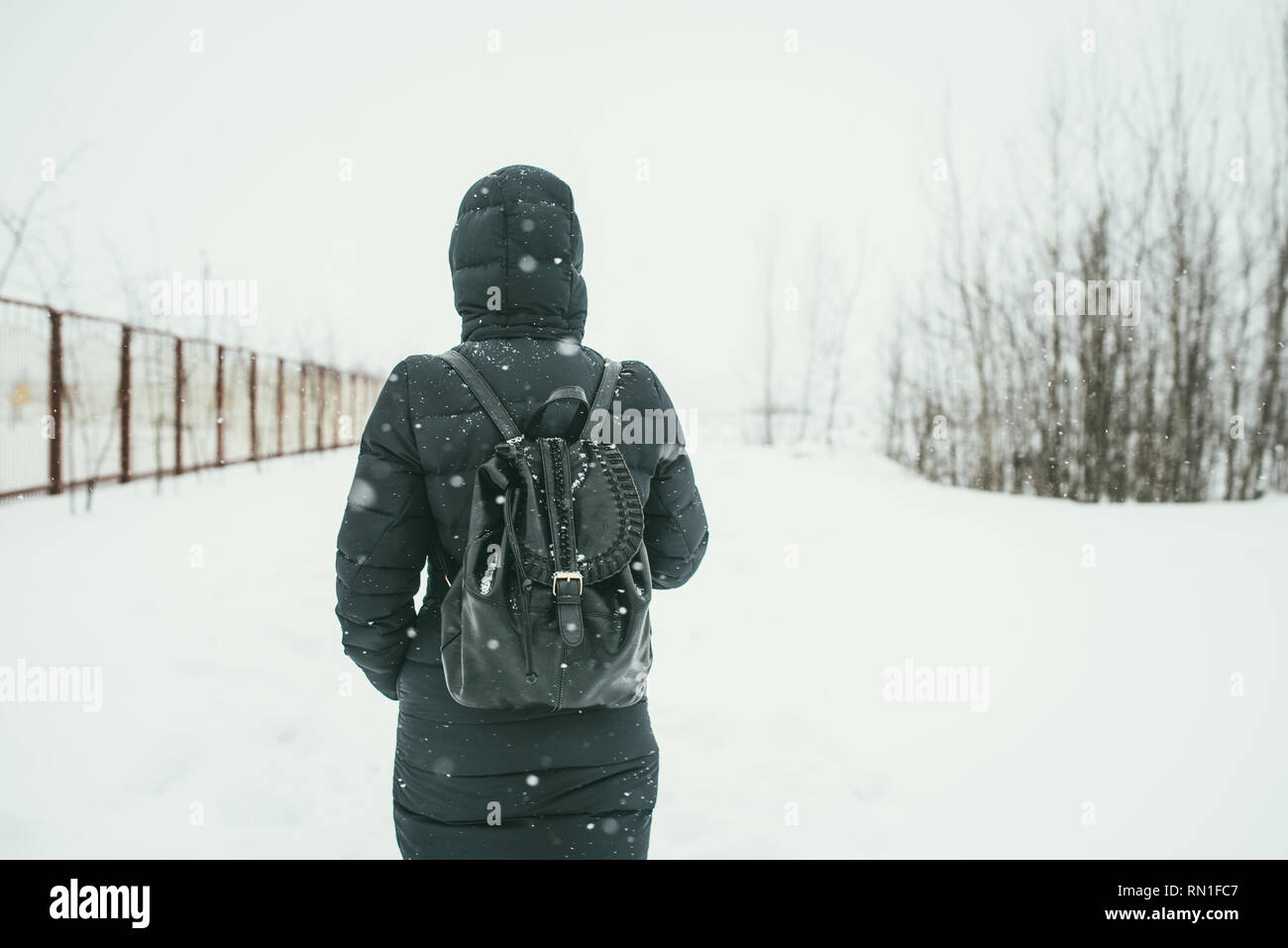 Un retour d'une belle shot youngwoman vêtu d'un manteau d'hiver noir avec sac à dos en cuir promenades dans la ville enneigée Banque D'Images