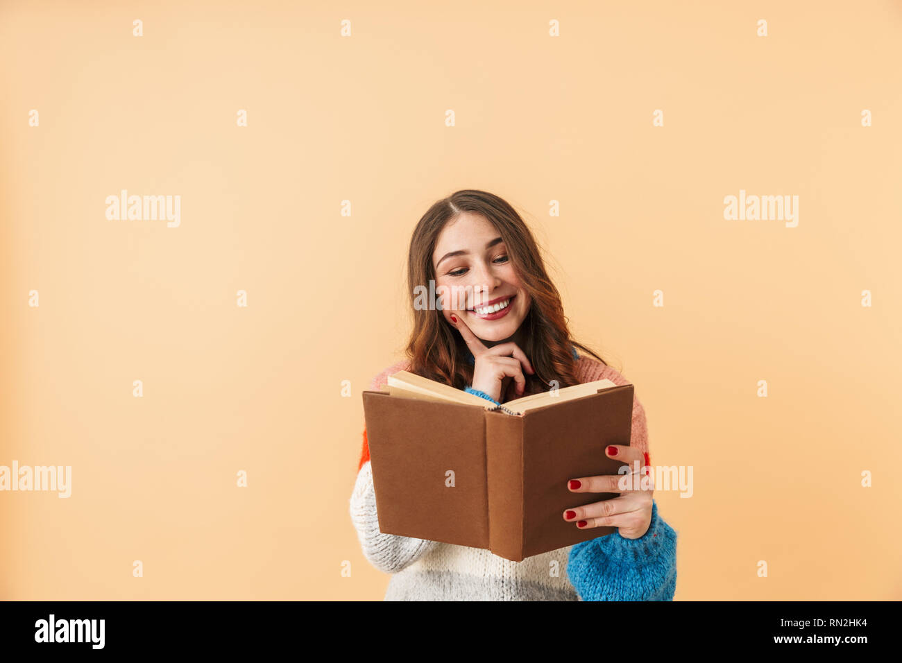 Image de femme brune 20s avec de longs cheveux smiling and reading book isolés sur fond beige Banque D'Images