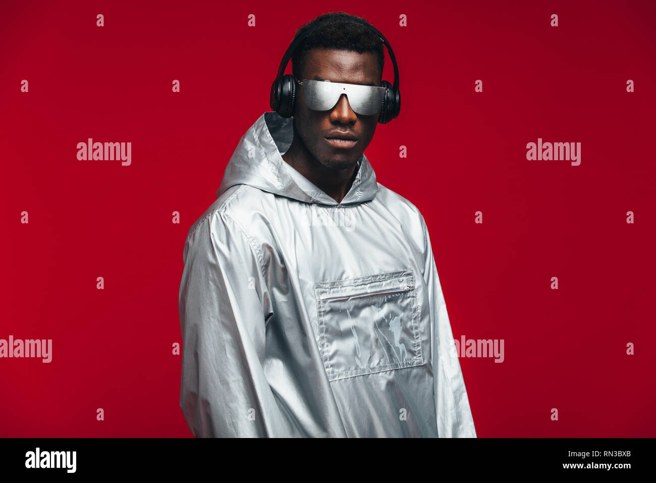 L'Afrique de l'élégant homme portant un t-shirt d'argent, des lunettes et des écouteurs à l'arrière-plan rouge. Funky young african american guy. Banque D'Images