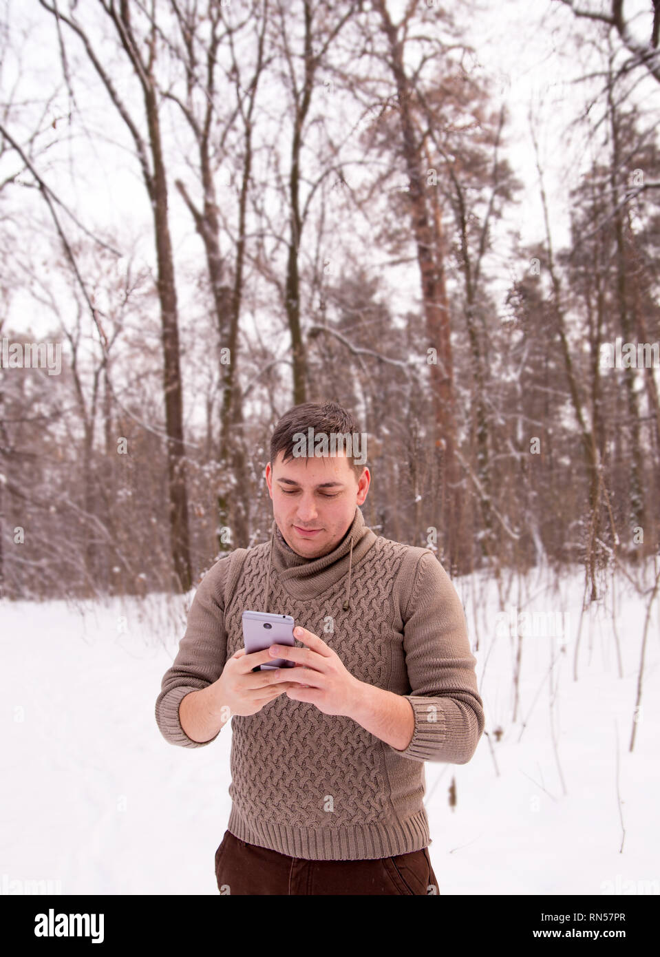 L'homme dans la forêt d'hiver fait une photo sur le téléphone. l'homme dans un pull en hiver dans les bois. Banque D'Images