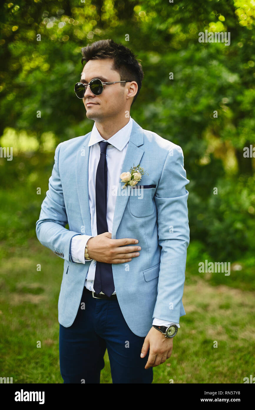 Handsome model homme portant dans le quartier à la veste bleue avec une  cravate et des lunettes de soleil élégante se trouve dans le jardin vert  Photo Stock - Alamy