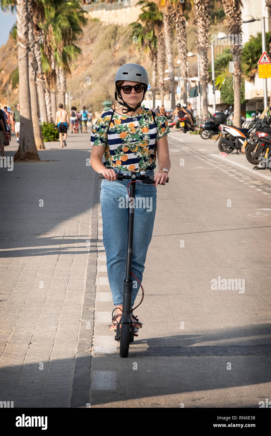 Une jolie jeune femme équitation un scooter électrique sur la piste cyclable Spitz Jim à Tel Aviv, près de la mer Méditerranée. Banque D'Images