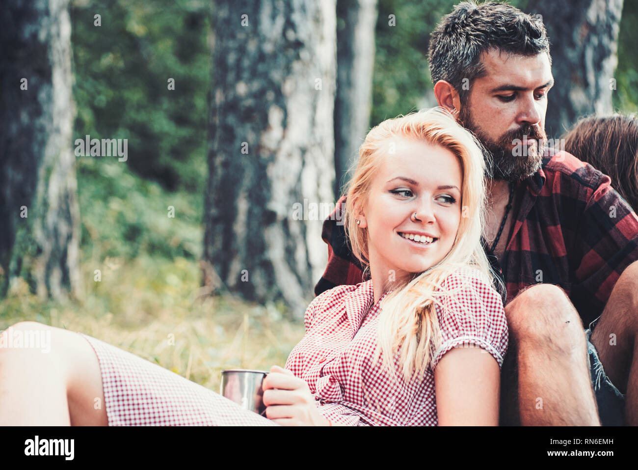 Fille blonde appuyée sur son petit ami. Groupe d'amis assis sur l'herbe à côté du feu de camp. Week-end romantique dans la nature Banque D'Images