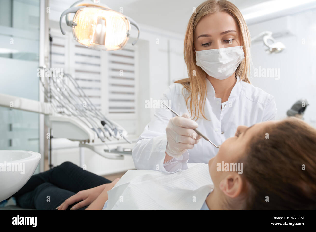 Dentiste professionnel médical portant des gants, masque et l'uniforme blanc. Votre médecin traitant du patient, la prévention des caries. Femme couchée dans dentiste président. Stomatologie concept. Banque D'Images