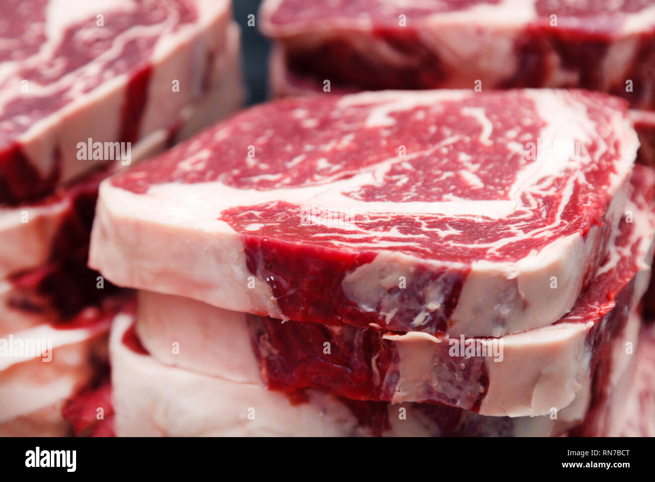 Pièces macro closeup Ribeye Steak de boeuf persillé sur la planche à découper en plastique rouge sur métal table dans une cuisine de restaurant. Concept de production semi-fini d'emballage Banque D'Images