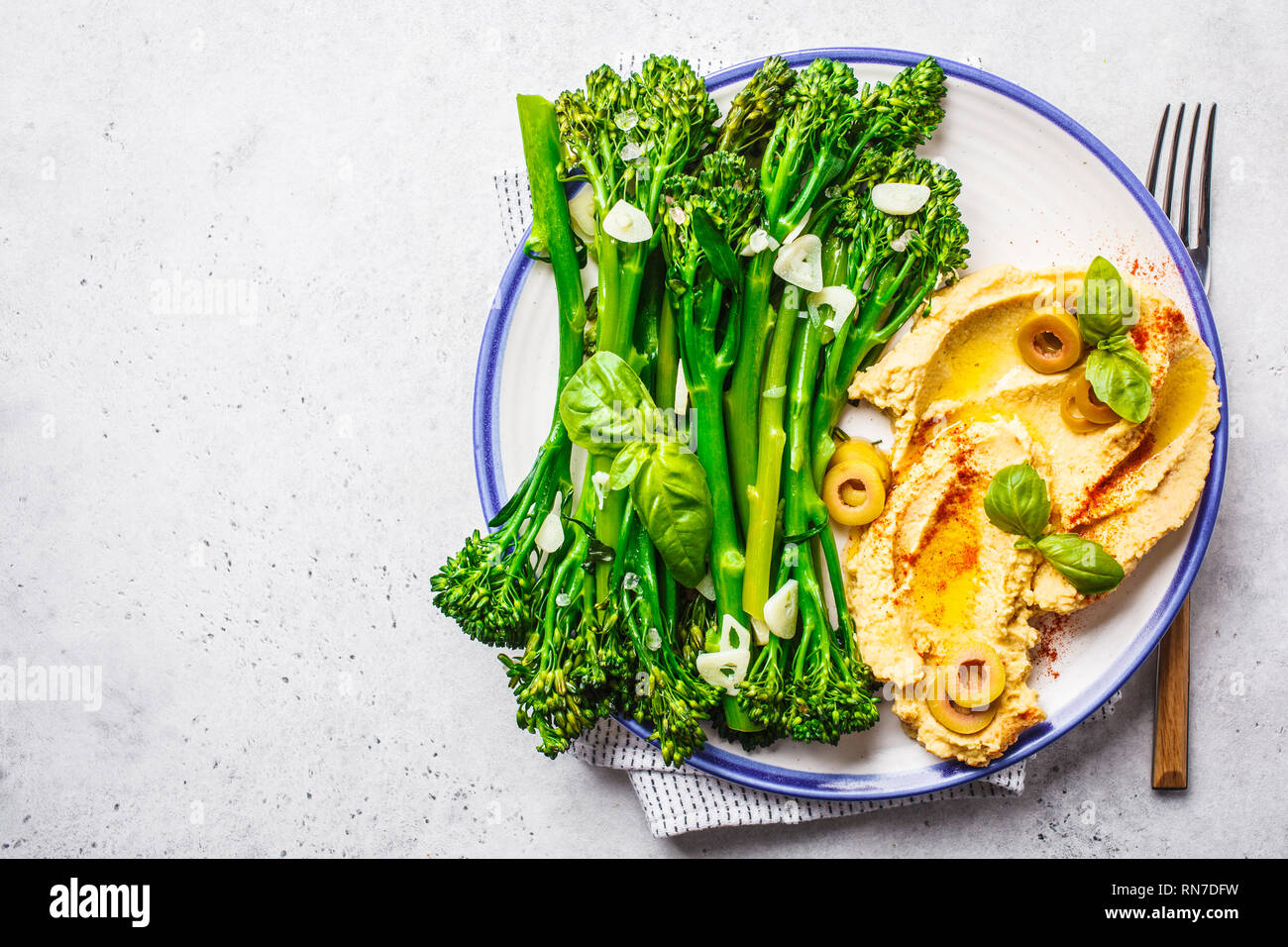 Broccolini cuit avec du hoummos sur une plaque blanche, vue du dessus. La nourriture végétalienne saine concept. Banque D'Images