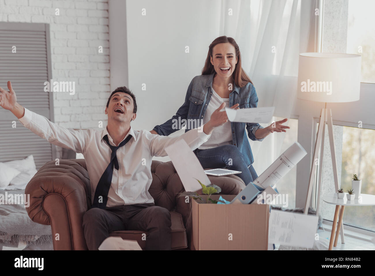 Ensemble avec succès. La famille émotionnelle joyeuse s'amusant à la maison tout en jetant en l'air et les documents en gardant leurs paumes vers le haut Banque D'Images