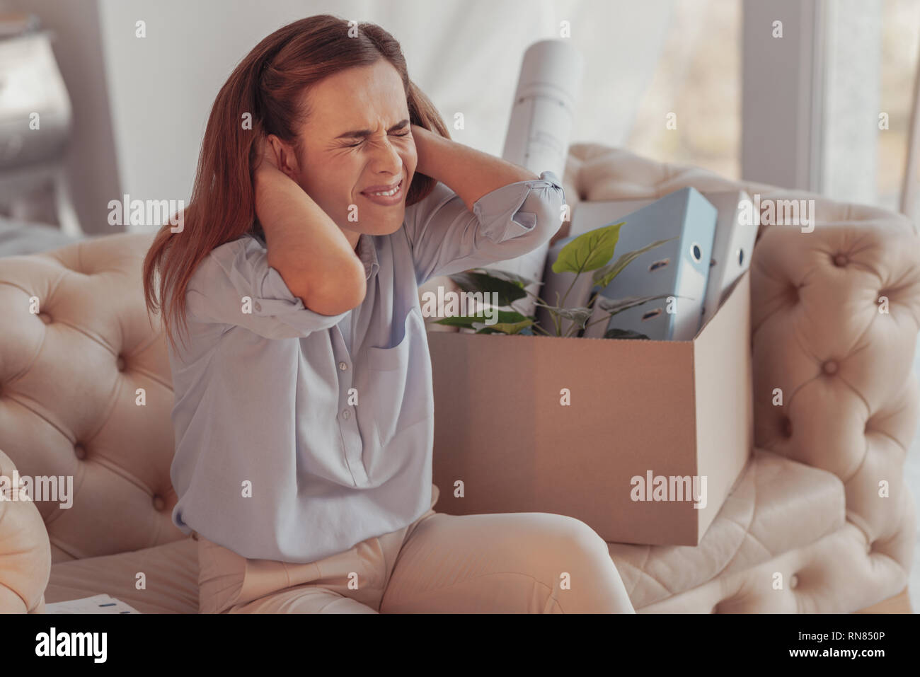 Assez. Portrait de jeune femme nerveux en gardant ses yeux fermés et son visage scrunching en touchant son cou annonce sitting on sofa Banque D'Images