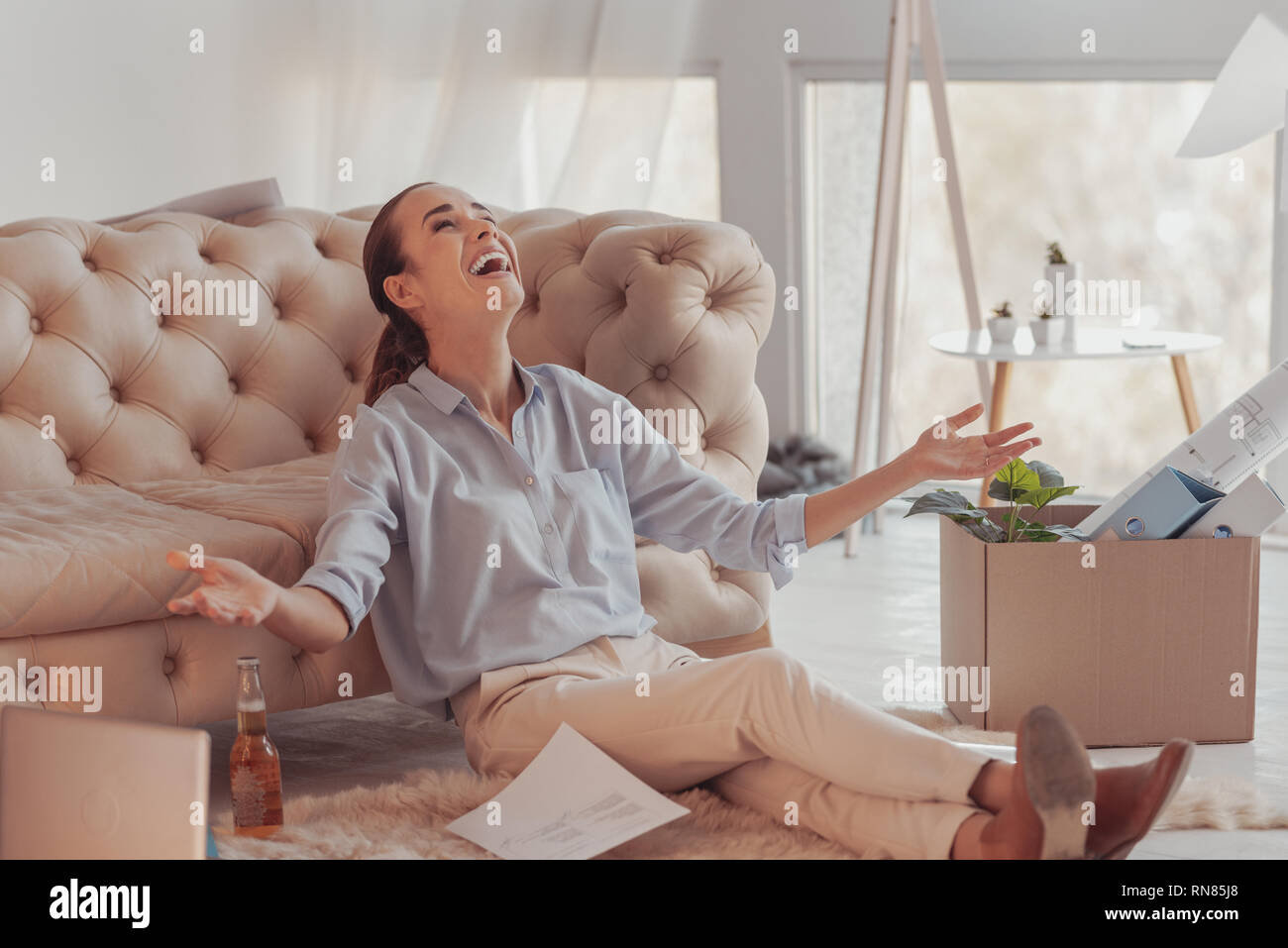 Succès pigiste. Longueur totale de jeunes heureux femme assise sur le sol et en maintenant ses paumes vers le haut tout en exprimant le bonheur et large sourire Banque D'Images