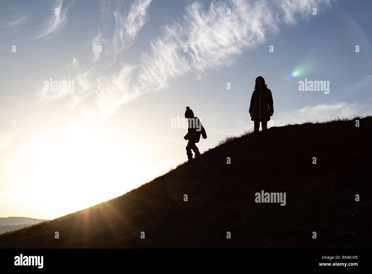 Grande soeur et enfant plus jeune frère l'ascension d'une colline dans l'arrière-light, silhouette Banque D'Images