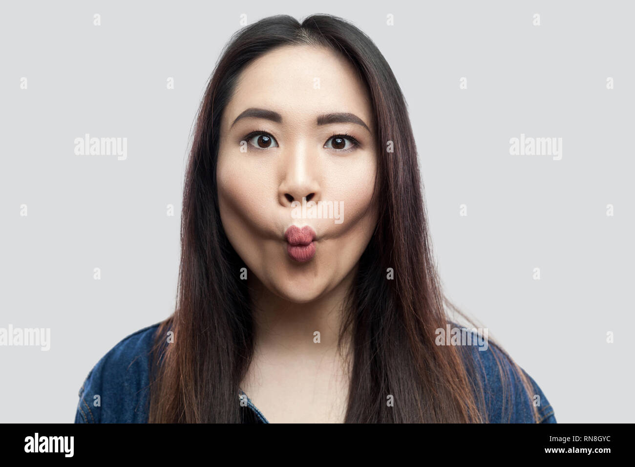 Portrait de funny belle brune asian young woman in casual veste en jean bleu avec un miroir debout avec de grands yeux et lèvres de poisson à l'intérieur st. Banque D'Images
