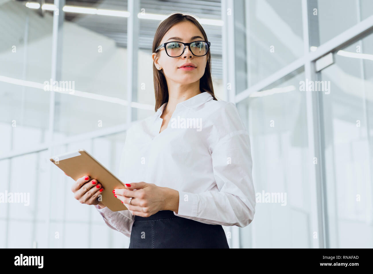 Attractive businesswoman using a digital tablet tout en se tenant dans un grand bâtiment de l'entreprise. Banque D'Images