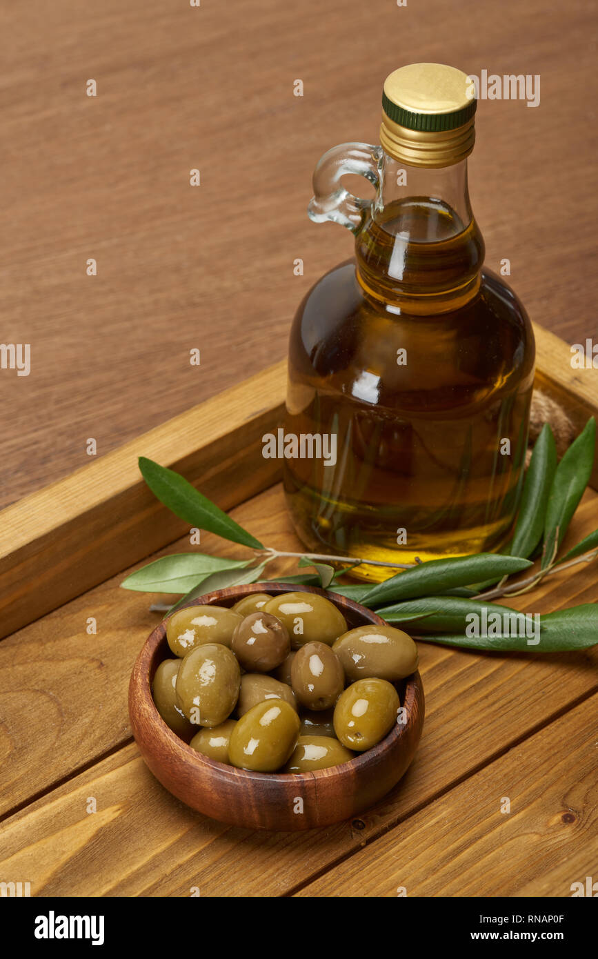 Plateau en bois avec une bouteille d'huile, bol d'olives et de feuilles d'arbres sur la surface brun Banque D'Images