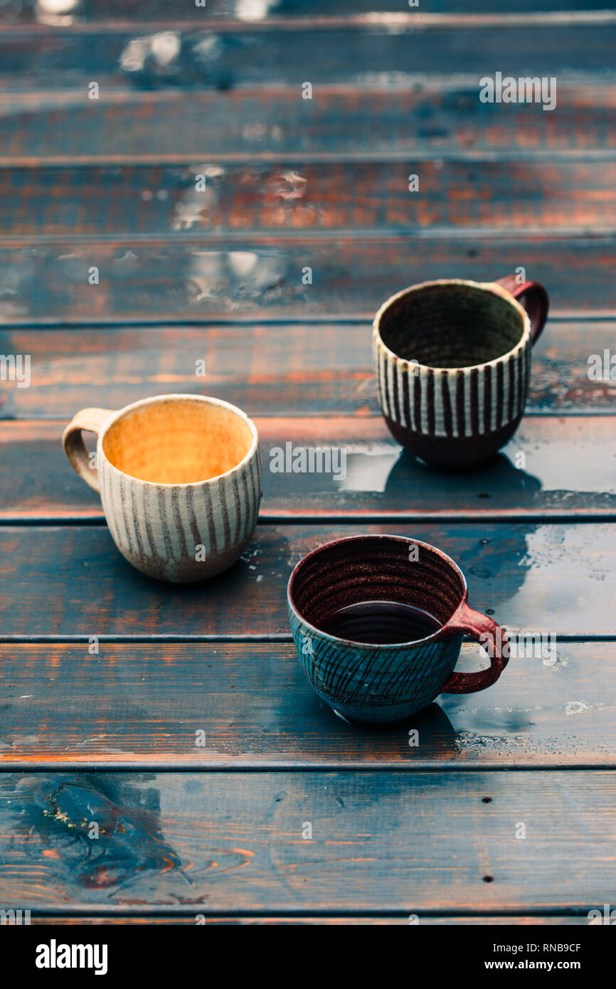 Un couple de tasses en terre avec du café et tisanes en bois sur table humide après la pluie Banque D'Images