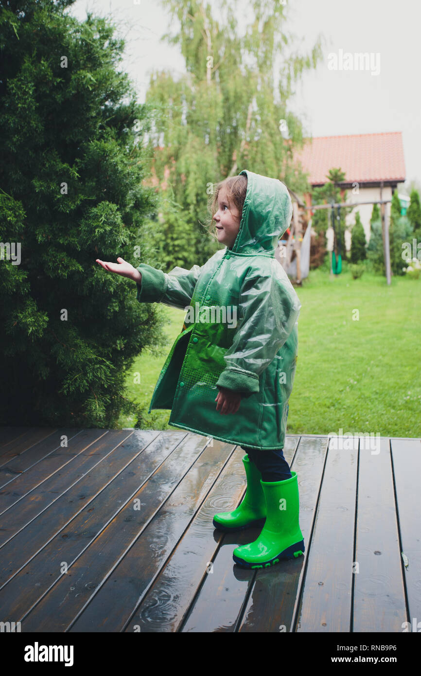 Happy smiling little girl debout sur un porche attraper les gouttes de pluie vert port Banque D'Images