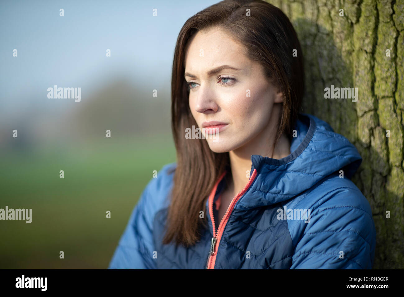 Malheureux à la Young Woman Leaning Against Tree On Winter Walk In Park Banque D'Images