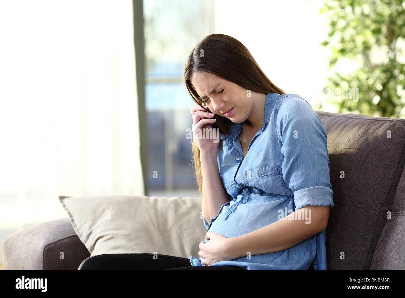Femme enceinte douloureux appelant médecin assis sur un canapé à la maison Banque D'Images