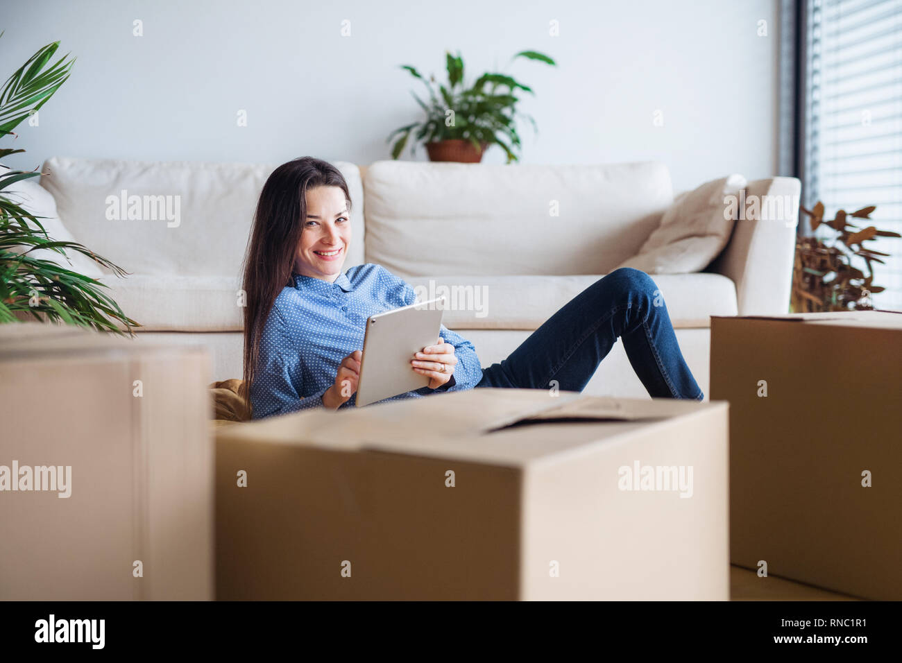 Une jeune femme avec tablet et boîtes de carton déménagement dans une nouvelle maison. Banque D'Images