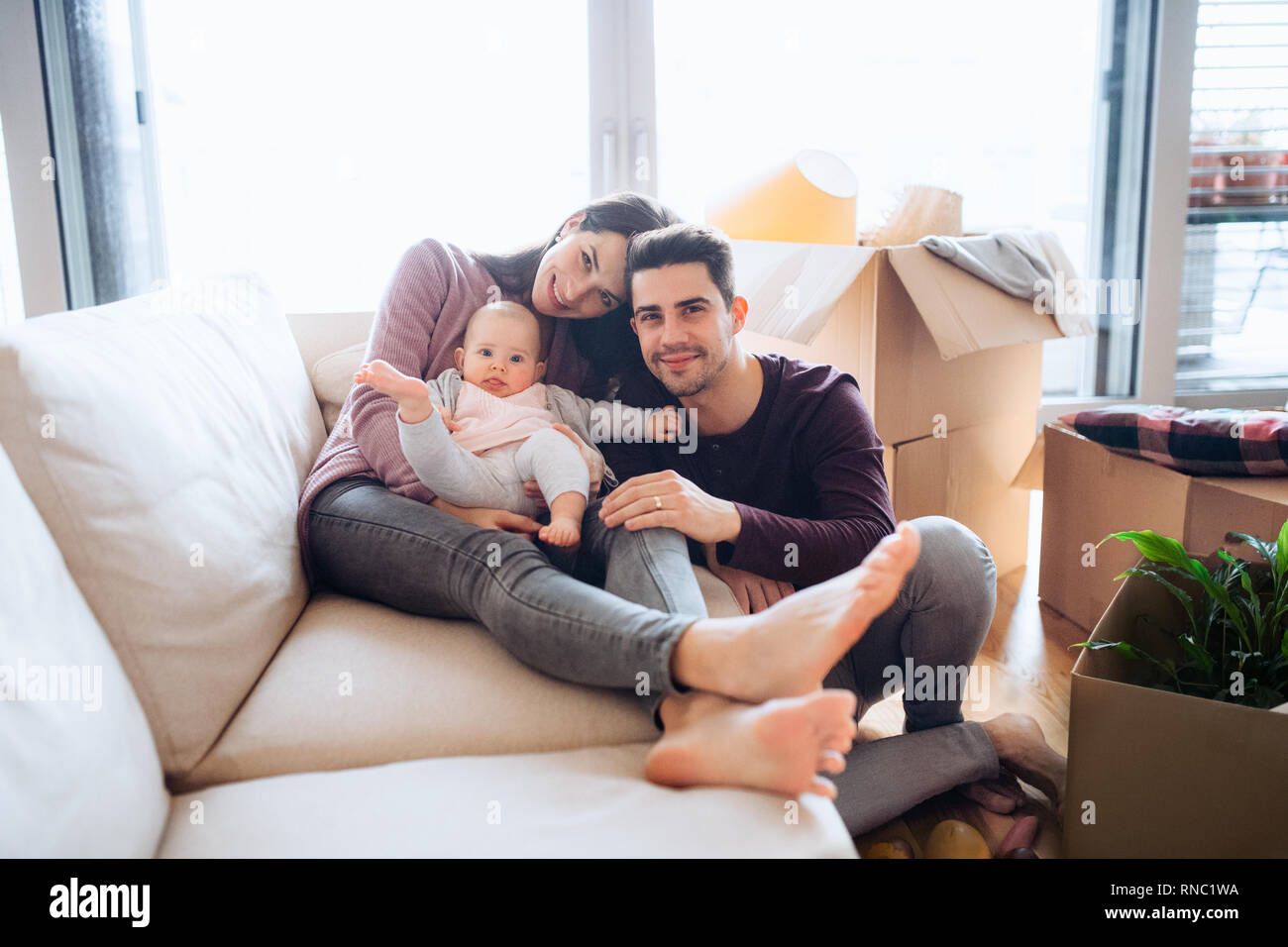 Portrait d'un jeune couple avec un bébé et des boîtes en carton déménagement dans une nouvelle maison. Banque D'Images