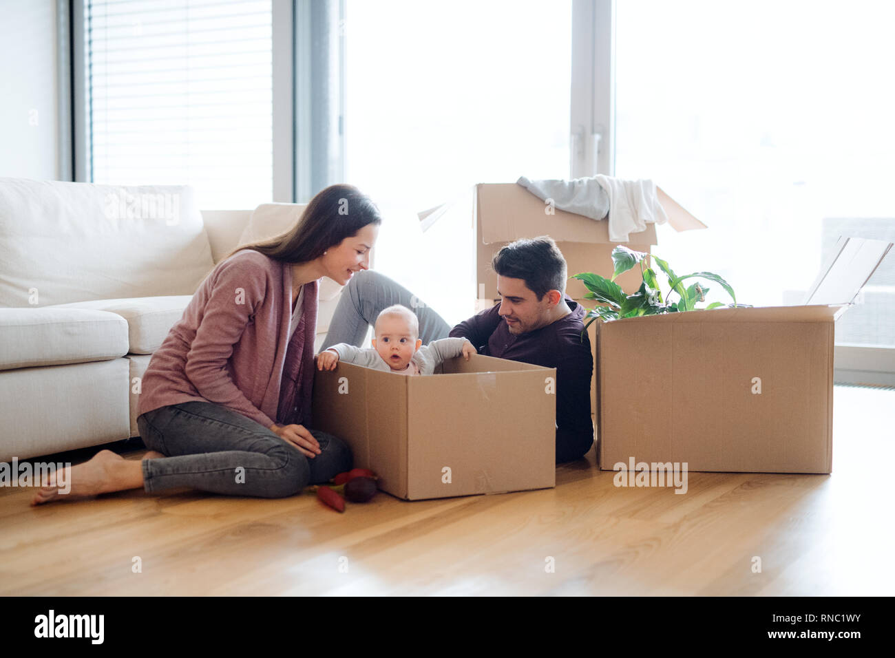 Portrait d'un jeune couple avec un bébé et des boîtes en carton déménagement dans une nouvelle maison. Banque D'Images