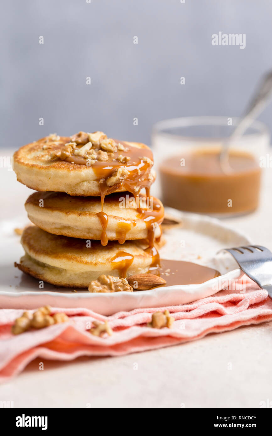 Pile de crêpes au caramel et noix sur la plaque blanche avec une serviette rose, sur un fond clair de fourche Banque D'Images Pile de crêpes au caramel et noix sur la plaque blanche avec une serviette rose, sur un fond clair de fourche Banque D'Images