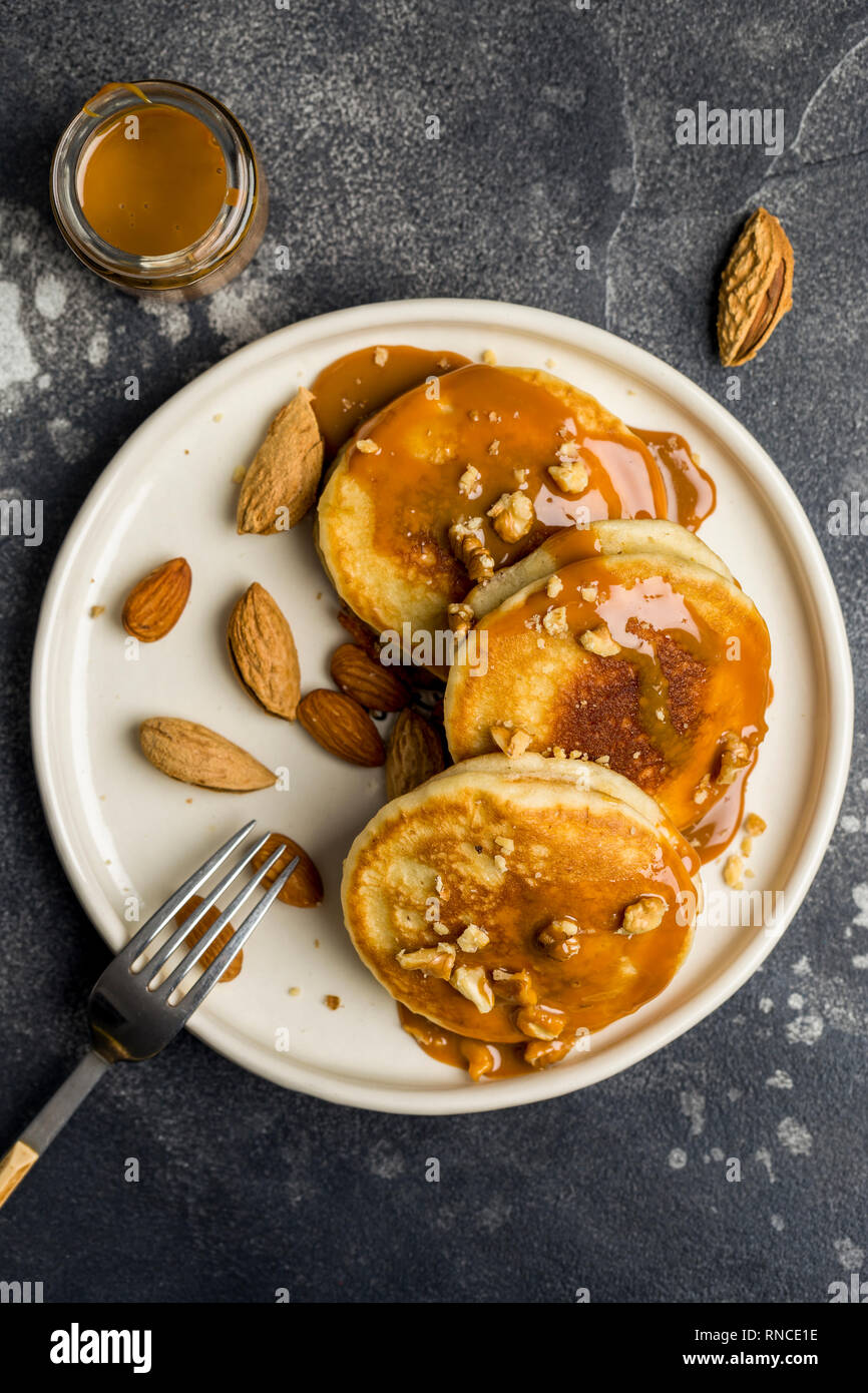 Espace libre vertical. Concept de petit-déjeuner américain avec des crêpes à la crème de caramel et noix sur fond sombre. Vue d'en haut Banque D'Images Espace libre vertical. Concept de petit-déjeuner américain avec des crêpes à la crème de caramel et noix sur fond sombre. Vue d'en haut Banque D'Images