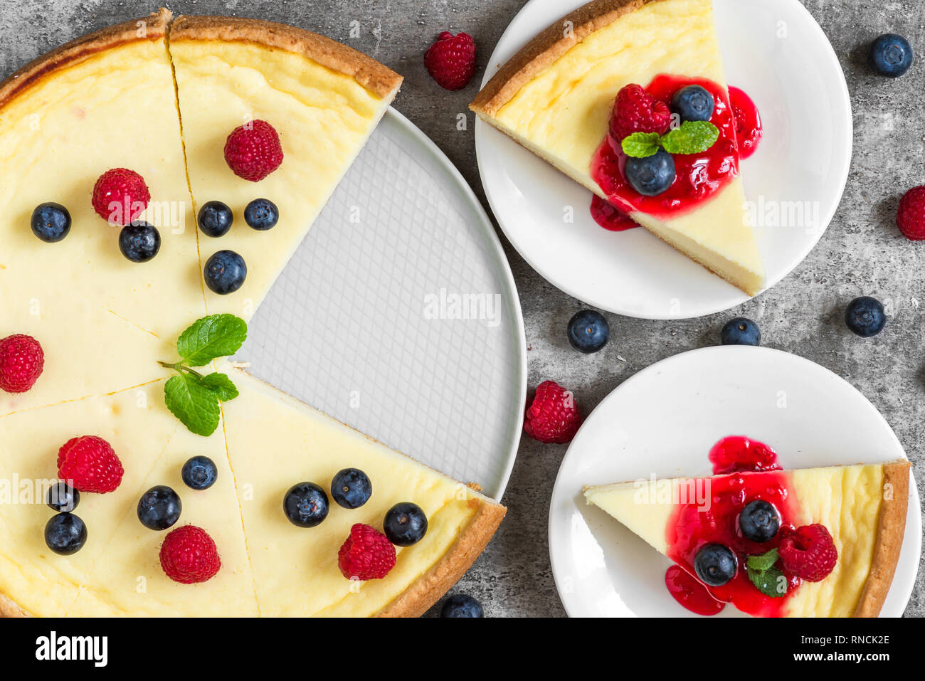 Gâteau au fromage avec deux tranches de gâteau avec les framboises, bleuets, de confiture et de menthe sur fond de béton. vue d'en haut. Bon petit déjeuner Banque D'Images