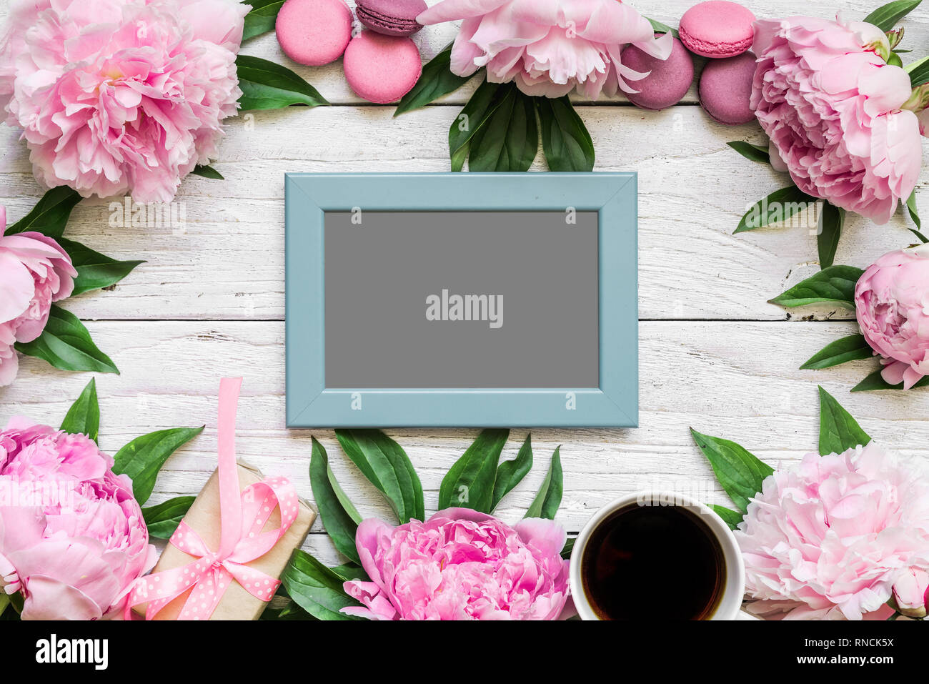 Carte photo vierge dans cadre fait de fleurs de pivoine rose, macarons et café tasse blanche sur fond de bois. Télévision. vue d'en haut.. la maquette ou mariage f Banque D'Images
