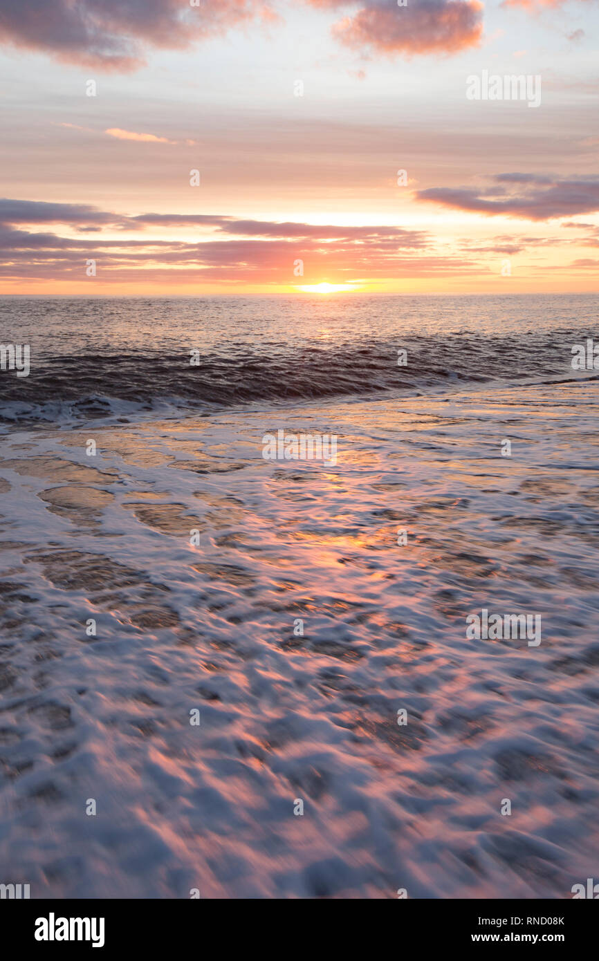 Vue à partir de la plage de Chesil près d'Abbotsbury en février le coucher de soleil avec des vagues écumeuses remué par de forts vents quelques jours avant, dans le foregrou Banque D'Images