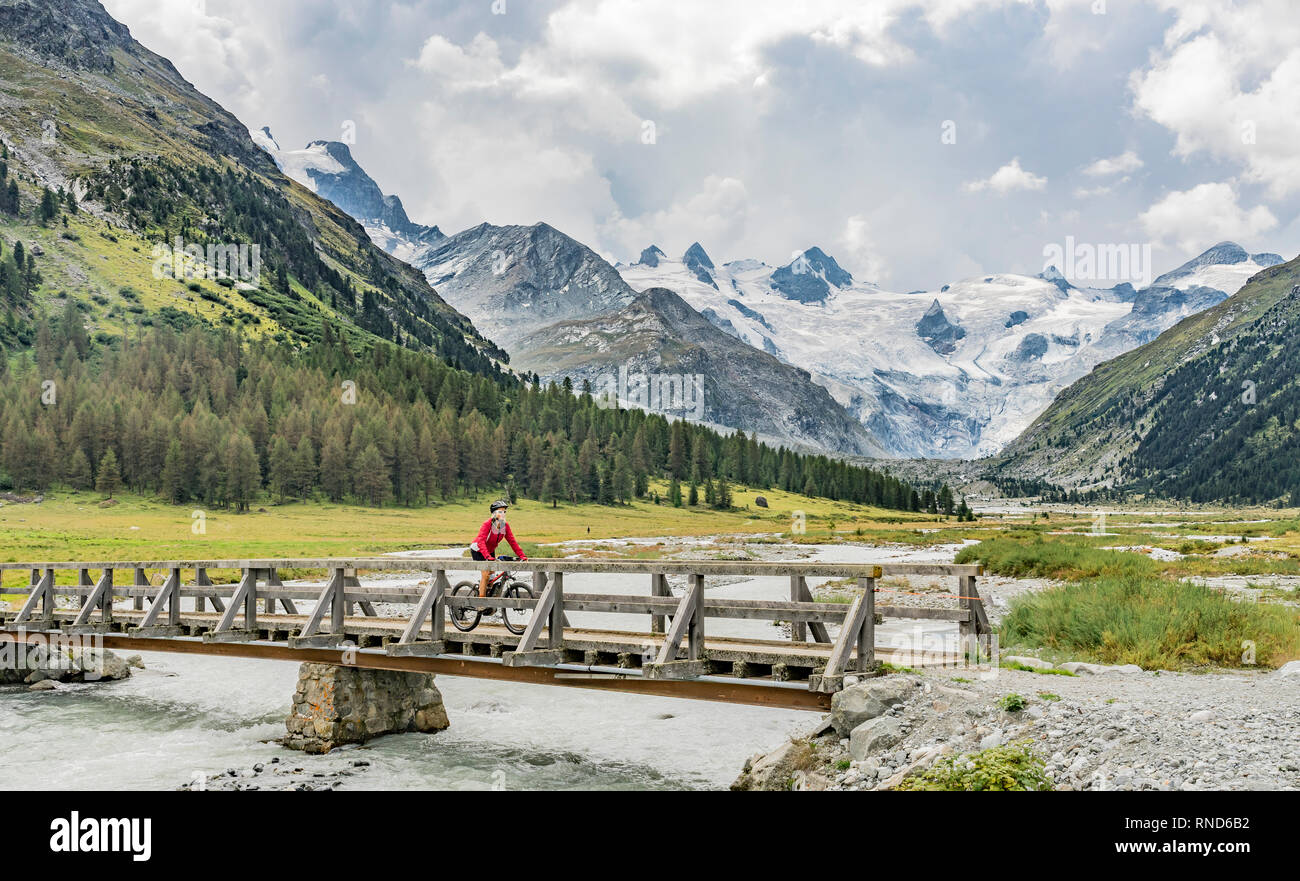 Active senior woman riding, son e-vtt dans la vallée de Roseg ci-dessous les glaciers et sommets de la Groupe du Sella et Piz Roseg Banque D'Images