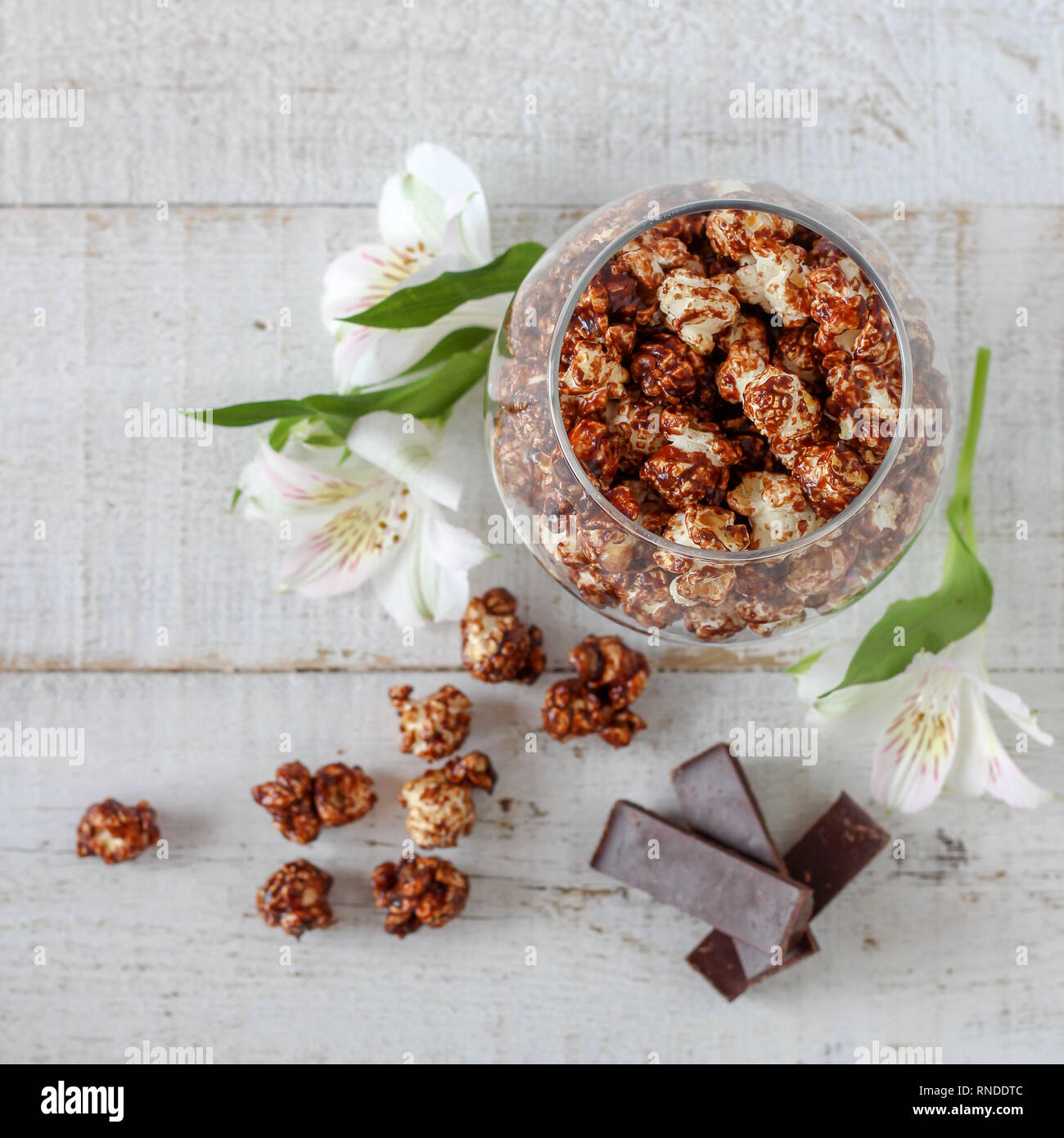 Maïs soufflé au chocolat et morceaux de chocolat et de fleurs sur une table en bois Banque D'Images