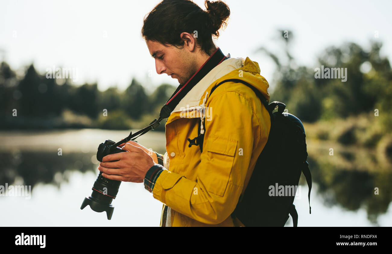 Vue latérale d'un touristiques à proximité d'un lac à la recherche de son appareil photo reflex numérique. Close up d'un voyageur à la recherche de son appareil photo numérique à l'extérieur permanent. Banque D'Images