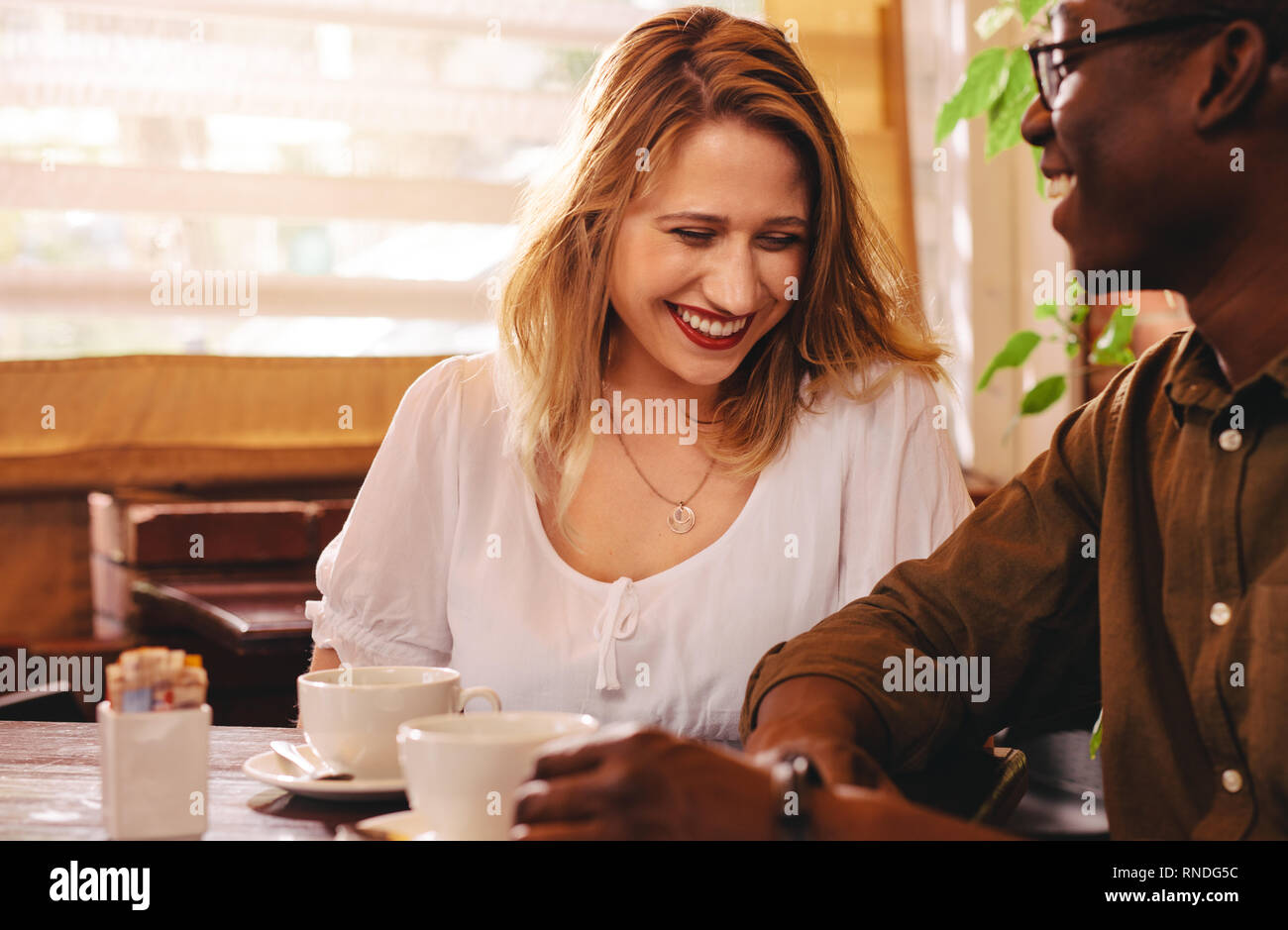 Cheerful woman sitting at cafe table avec son petit ami. Multi-ethnic couple ensemble au café. Banque D'Images