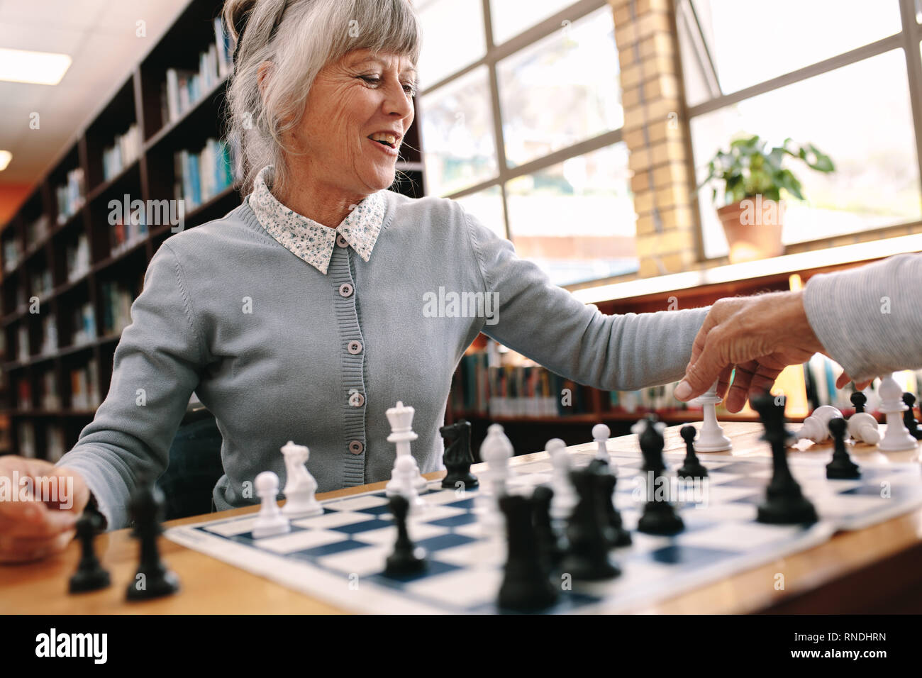 Hauts femme jouant un jeu d'échecs avec son partenaire. Cheerful woman relaxing jouant aux échecs. Banque D'Images