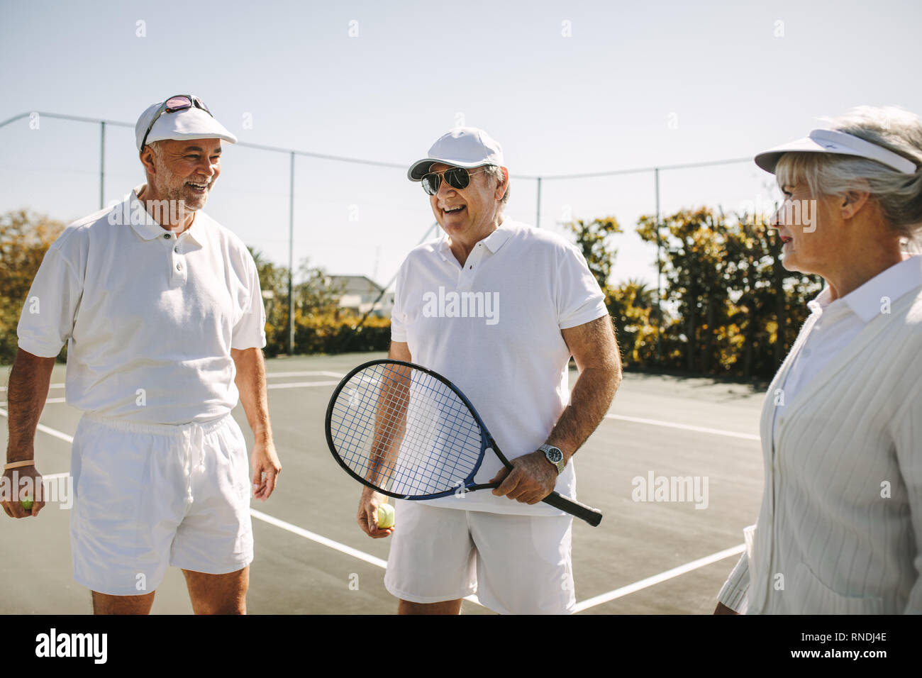 Les personnes jouant au tennis sur une journée ensoleillée. Cheerful old men standing on tennis holding racket et de balles. Banque D'Images