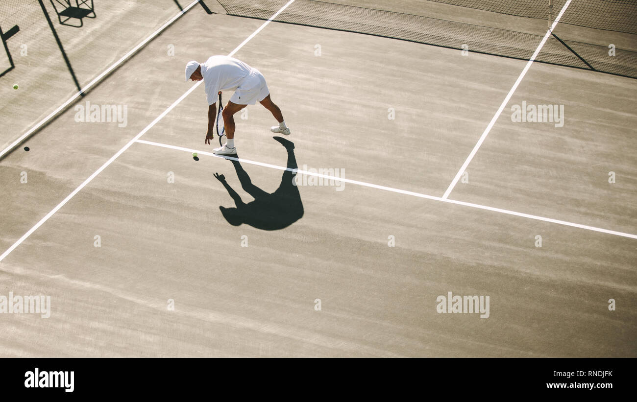 Vue aérienne d'un homme jouant au tennis sur une journée ensoleillée. Vue de dessus d'un homme en se penchant pour ramasser une balle de tennis. Banque D'Images