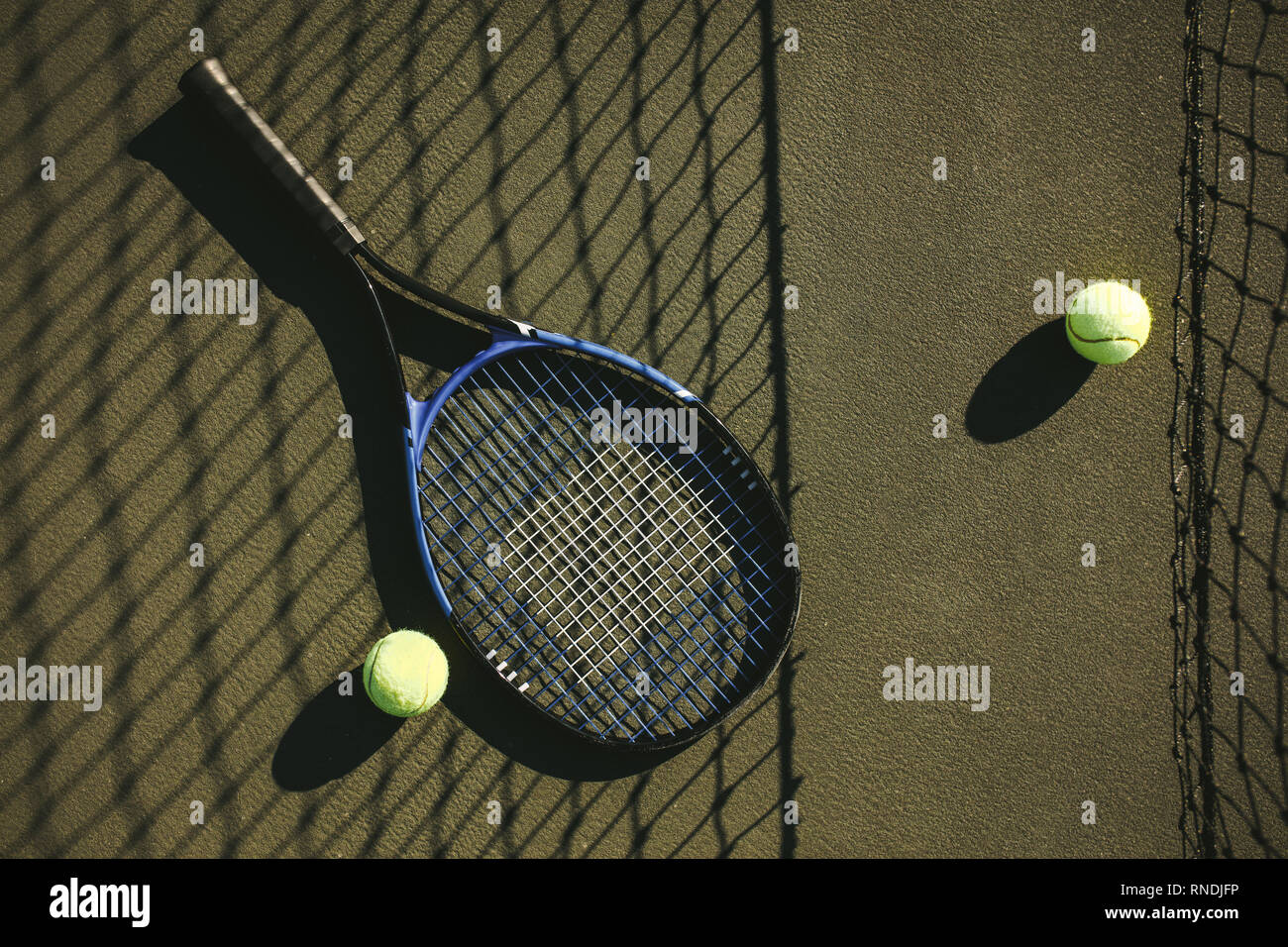 Gros plan d'une raquette de tennis et de balles gisant sur le court. raquette de tennis et balles placées à côté d'un filet sur un court de tennis par une journée ensoleillée. Banque D'Images