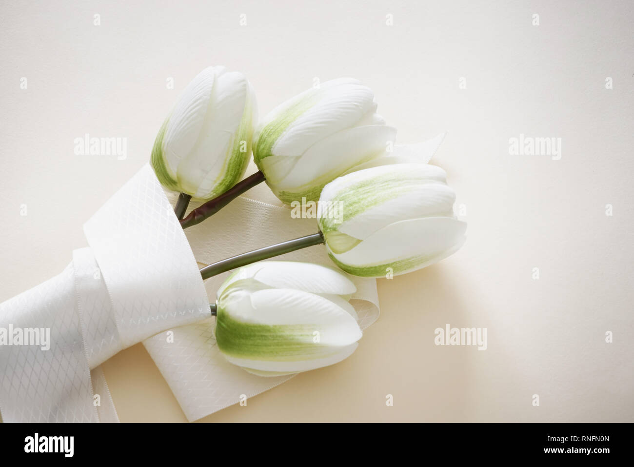 Joli bouquet de tulipes blanches artificiel enveloppé de ruban dans l'arrière-plan de couleur pastel. Concept de la Fête des mères avec l'exemplaire de l'espace. Banque D'Images