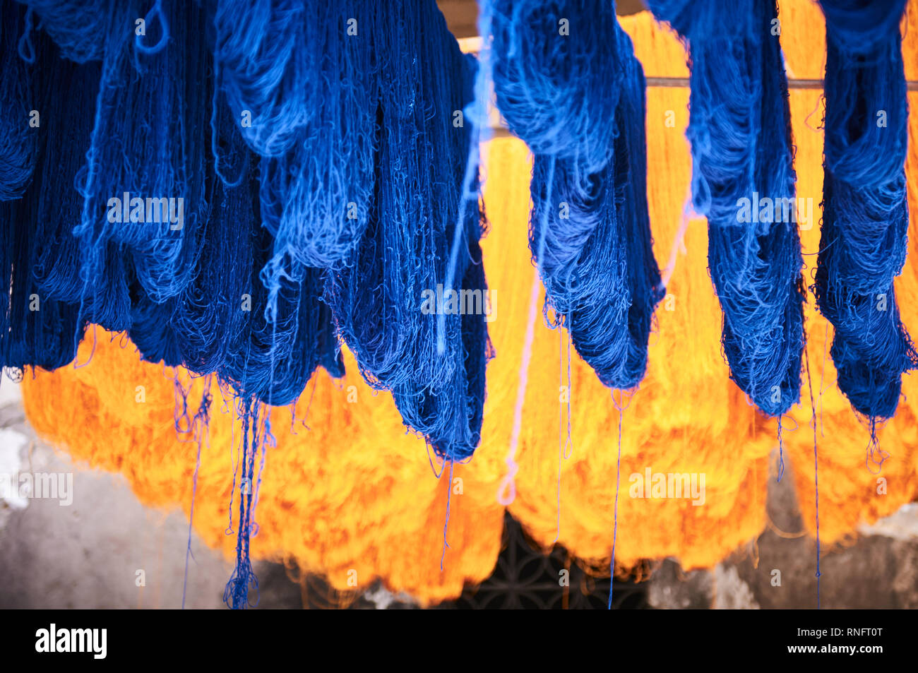 Des paquets de chaîne de laine accroché les poteaux de bambou frais généraux à sécher au soleil dans le district de teinture les rues de Marrakech. Banque D'Images
