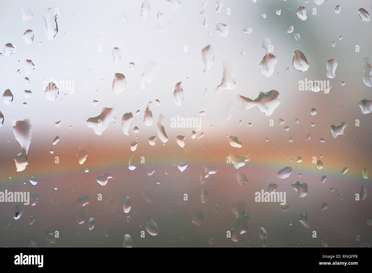 Les lumières colorées d'un arc-en-ciel derrière une vitre avec des gouttes de pluie. Banque D'Images