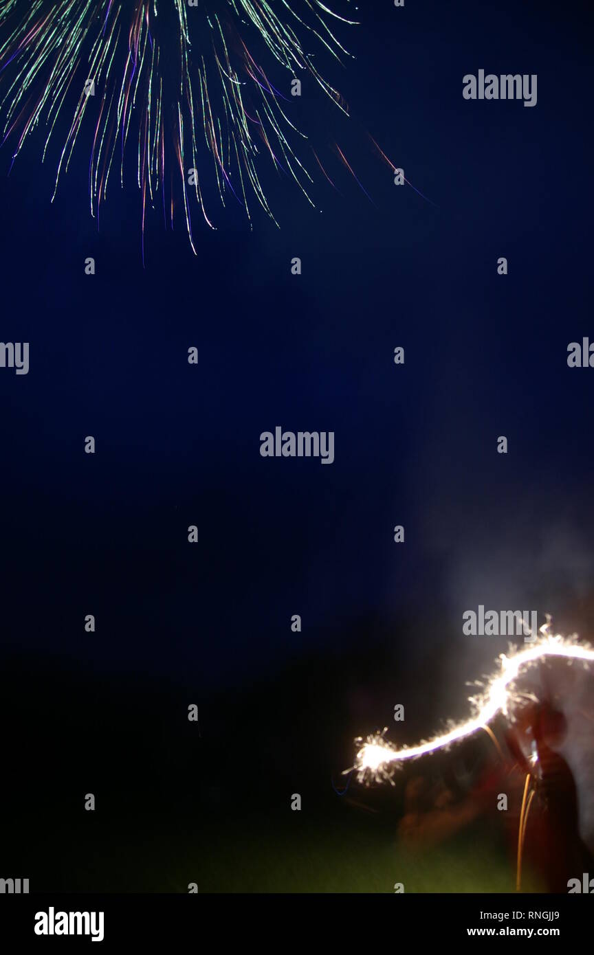 Silhouette d'enfant avec burning sparkler la nuit dans le coin inférieur droit, feu d'artifice éclatant dans le coin supérieur gauche. Quatrième de juillet, Fête de l'indépendance US Banque D'Images