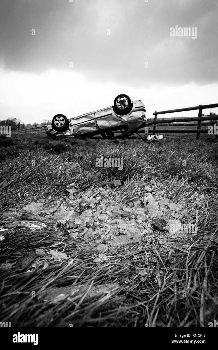 Accident de voiture et location de dommages. Véhicule à l'envers dans un champ entouré par des éclats de verre et les débris après une collision à haute vitesse. Banque D'Images