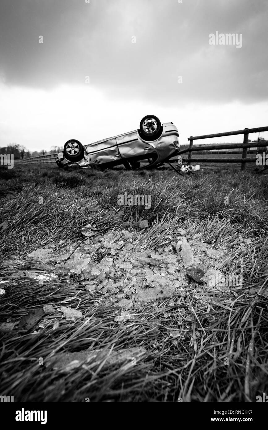 Accident de voiture et location de dommages. Véhicule à l'envers dans un champ entouré par des éclats de verre et les débris après une collision à haute vitesse. Banque D'Images