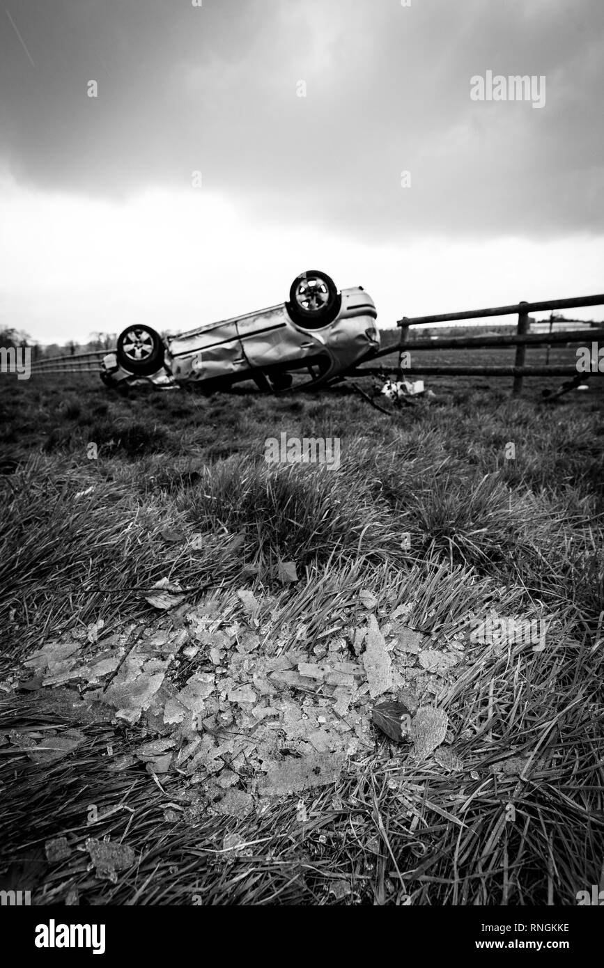 Accident de voiture et location de dommages. Véhicule à l'envers dans un champ entouré par des éclats de verre et les débris après une collision à haute vitesse. Banque D'Images