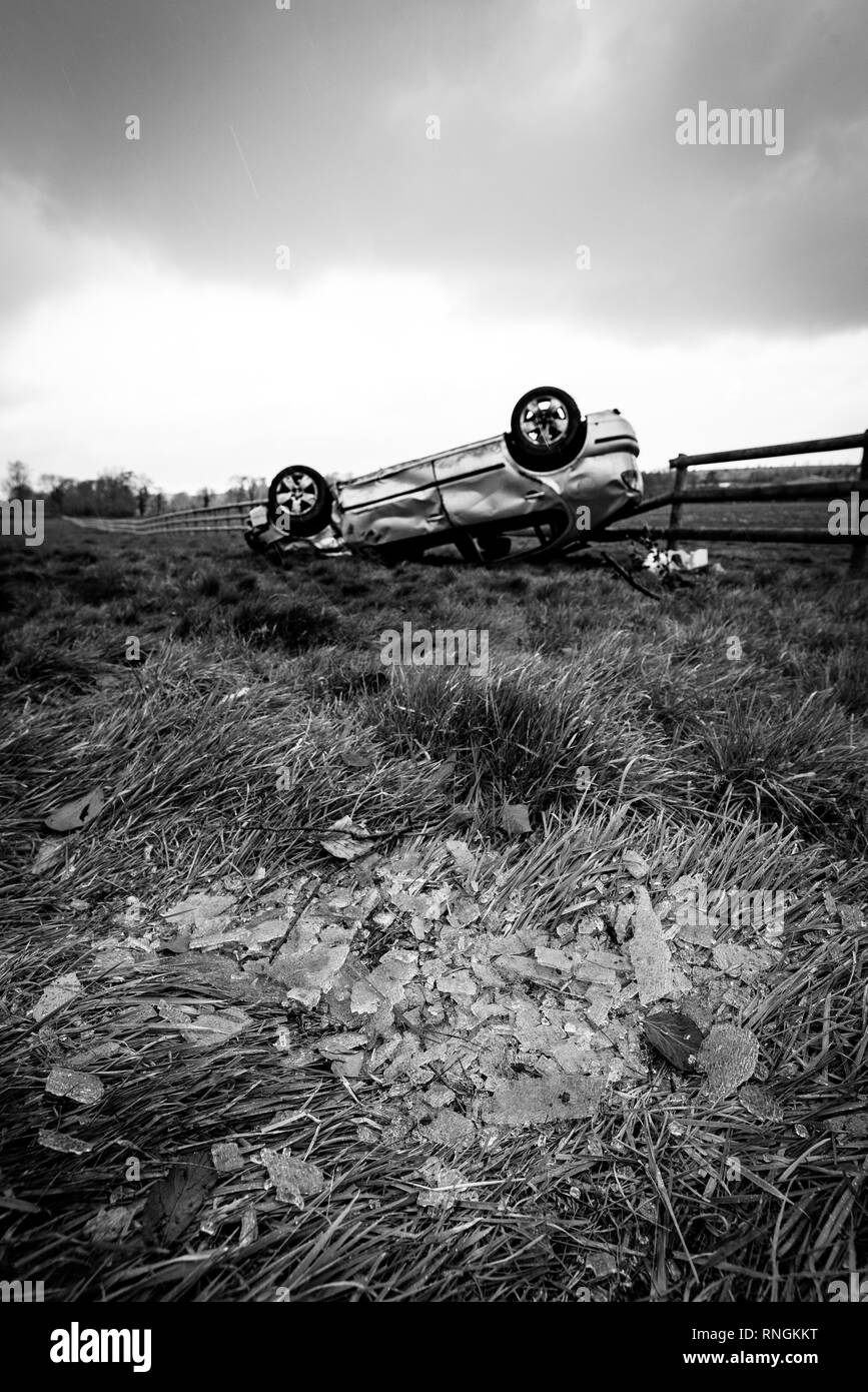 Accident de voiture et location de dommages. Véhicule à l'envers dans un champ entouré par des éclats de verre et les débris après une collision à haute vitesse. Banque D'Images