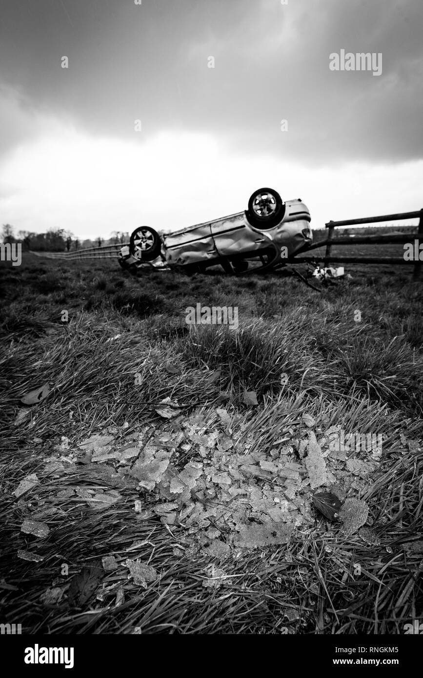 Accident de voiture et location de dommages. Véhicule à l'envers dans un champ entouré par des éclats de verre et les débris après une collision à haute vitesse. Banque D'Images
