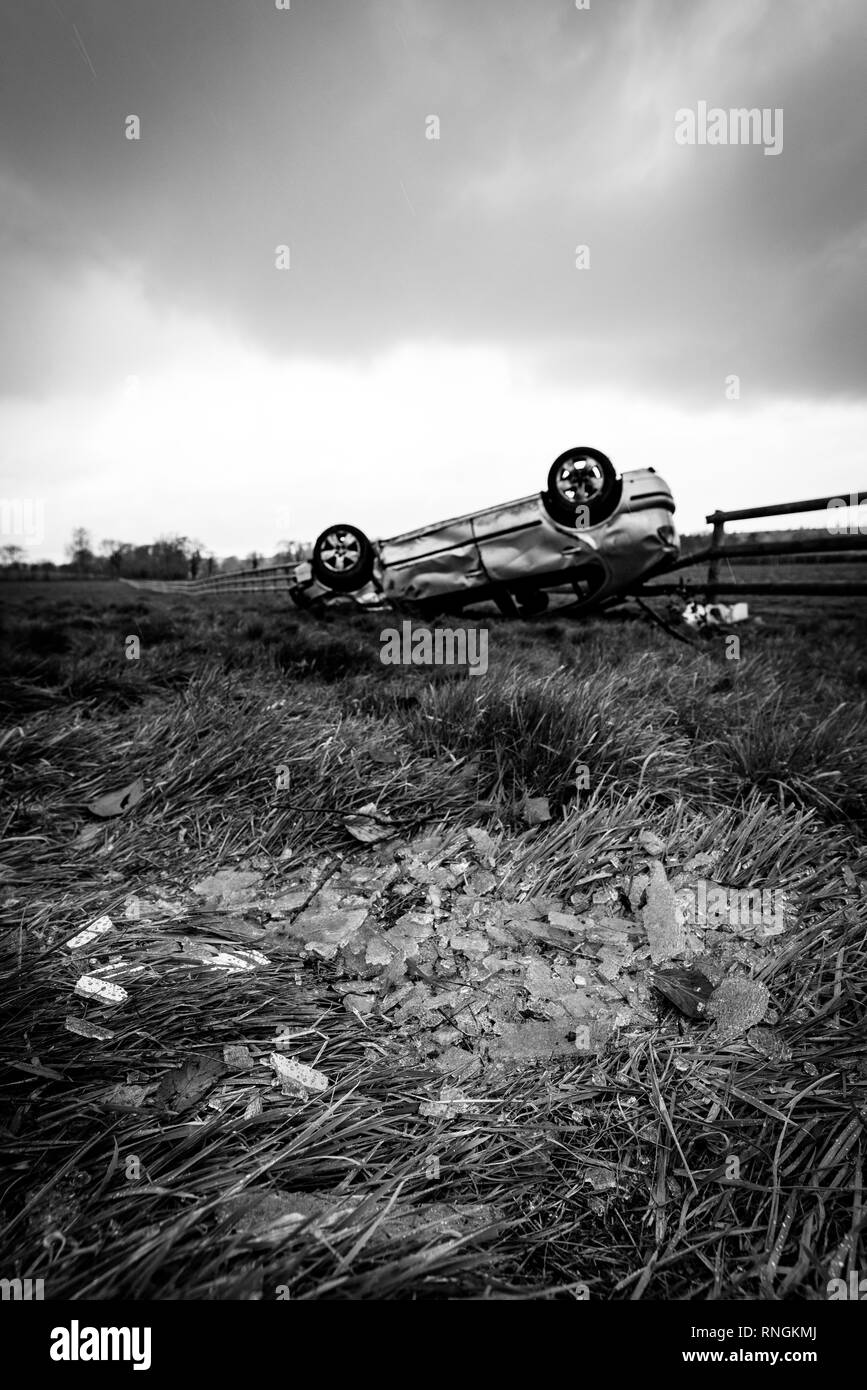 Accident de voiture et location de dommages. Véhicule à l'envers dans un champ entouré par des éclats de verre et les débris après une collision à haute vitesse. Banque D'Images