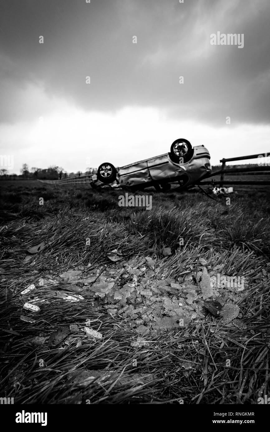 Accident de voiture et location de dommages. Véhicule à l'envers dans un champ entouré par des éclats de verre et les débris après une collision à haute vitesse. Banque D'Images