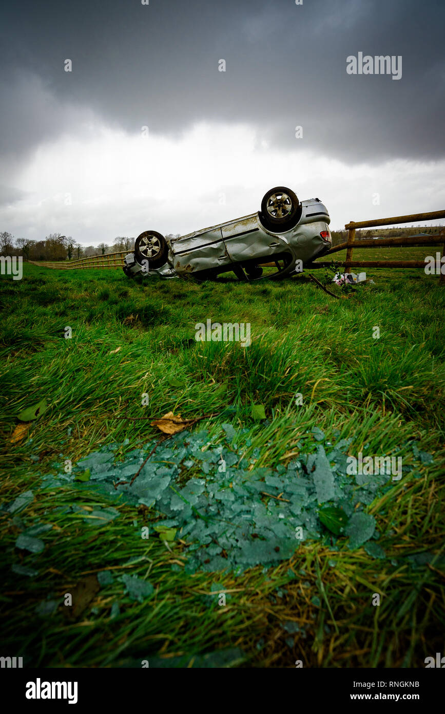 Accident de voiture et location de dommages. Véhicule à l'envers dans un champ entouré par des éclats de verre et les débris après une collision à haute vitesse. Banque D'Images