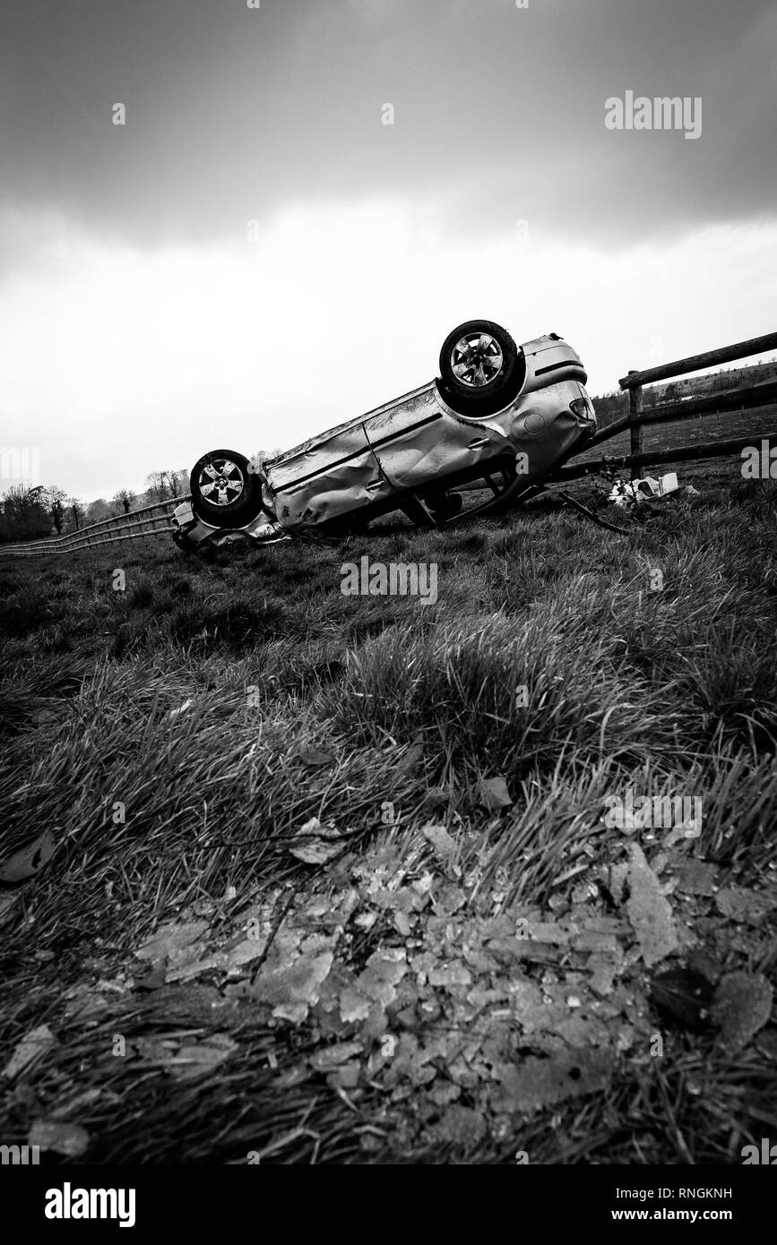 Accident de voiture et location de dommages. Véhicule à l'envers dans un champ entouré par des éclats de verre et les débris après une collision à haute vitesse. Banque D'Images